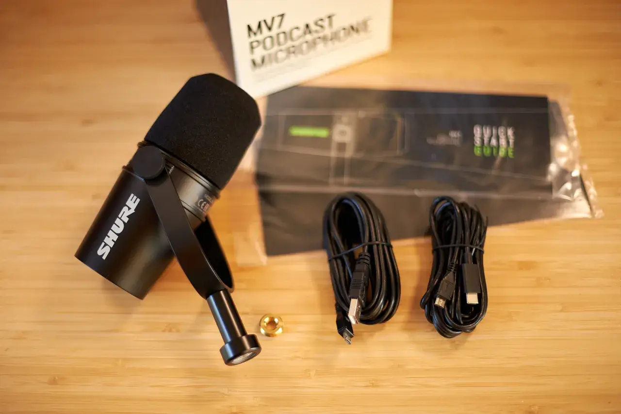 Das Mikrofon, das schwarz ist, zwei USB Kabel, ordentlich zusammen gefaltet, und ein goldener Gewindeadapter vom gro&szlig;en Gewinde der Halterung auf eine kleinere